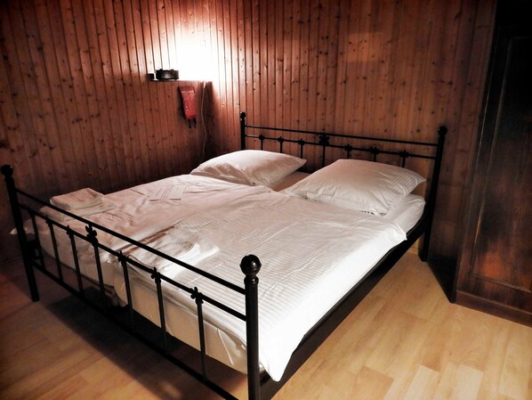 Un lit simple avec un cadre en métal, dans une pièce aux murs et au plancher en bois.