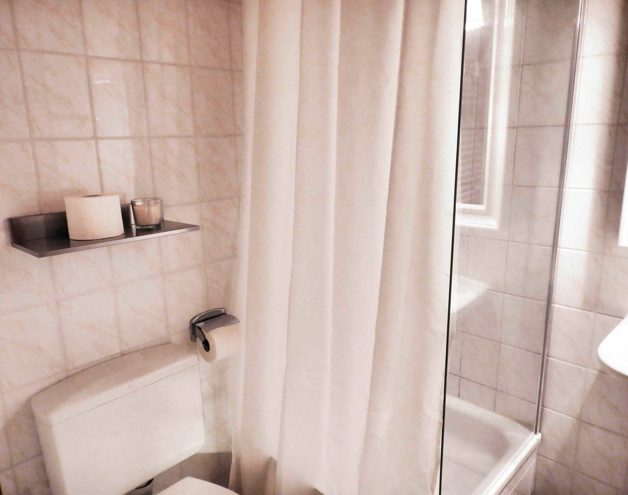 Ein Badezimmer mit Toilette, einem Ablagefach mit Toilettenpapier und einer Kerze, sowie einem Duschbereich mit Glastür.
