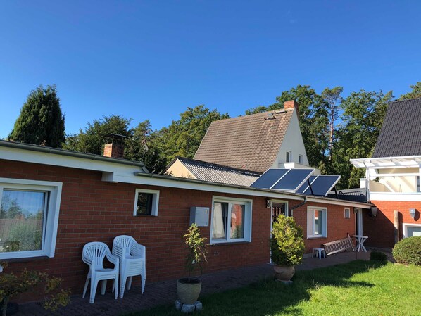 Ein Backsteinhaus mit Solaranlage, weißen Kunststoffstühlen und einem Blumentopf.
