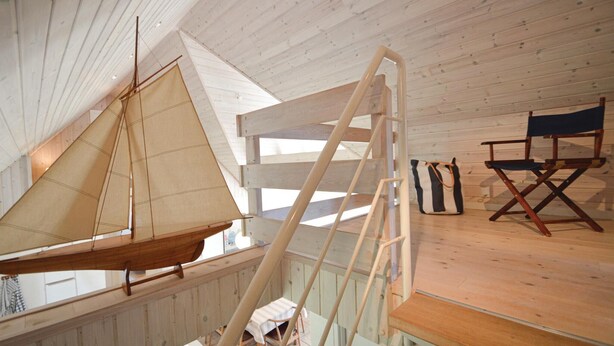 A sailboat in a wooden interior with a ladder, a director's chair, and a striped bag.