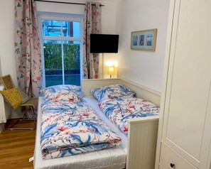 Camera da letto con due letti, tende floreali, televisione e lampada da comodino.