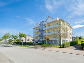 Un edificio residenziale a più piani con balconi, una strada pavimentata e presenza di verde.