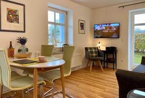 Un coin repas avec une table ronde, des chaises vertes et un téléviseur fixé au mur.