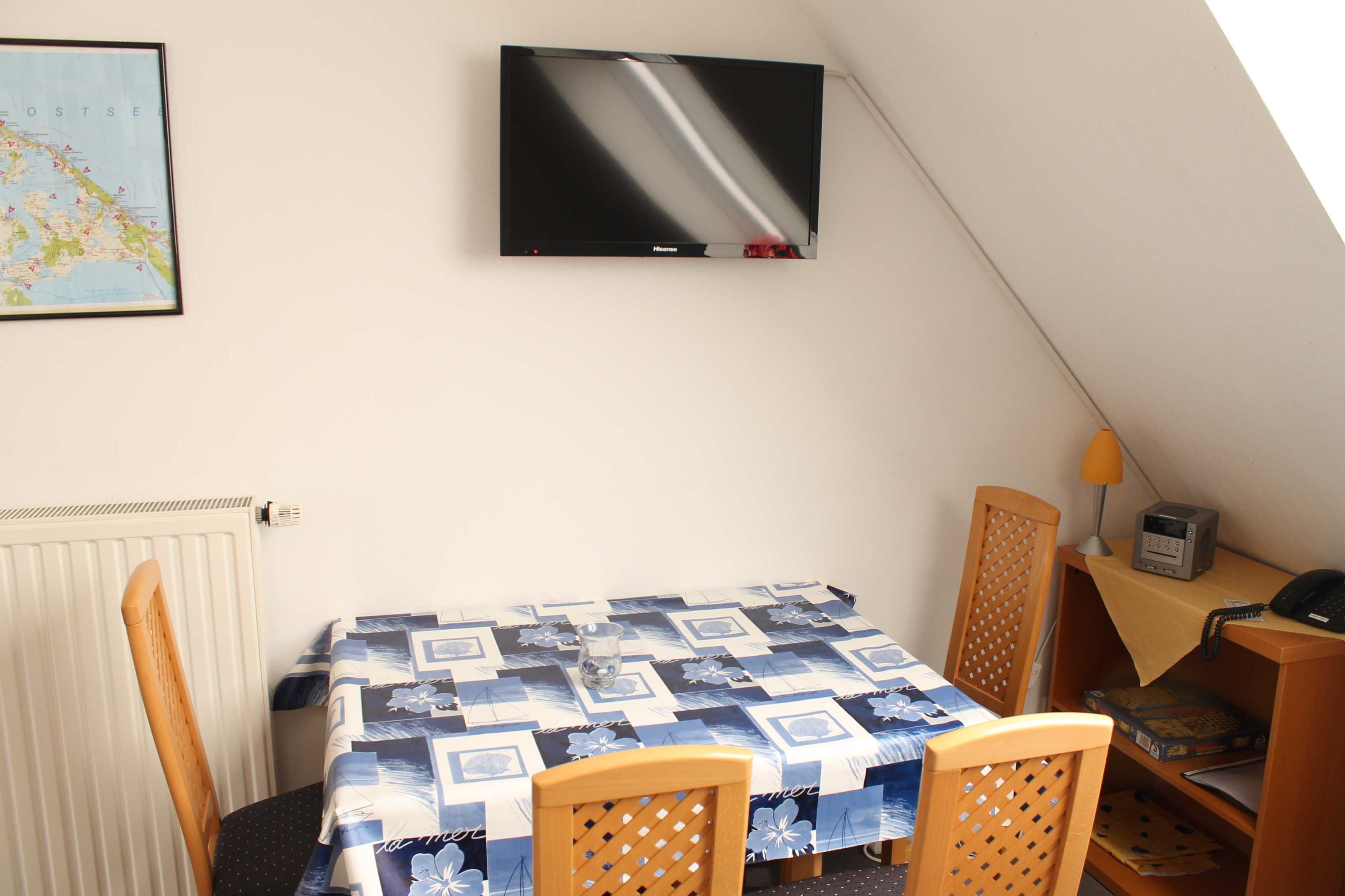 Une petite pièce agréable, avec une table et des chaises, un téléviseur fixé au mur et une carte accrochée au mur.