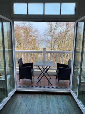 A glass-enclosed balcony with a table and two chairs, offering a view of trees and a clear sky. - (26) 2-room apartment Ostseeallee - apartment house dune castle (Kühlungsborn)