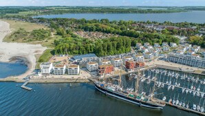 Oversigtsbillede af en kystby med lystbådehavn, boligbygninger og en strand.