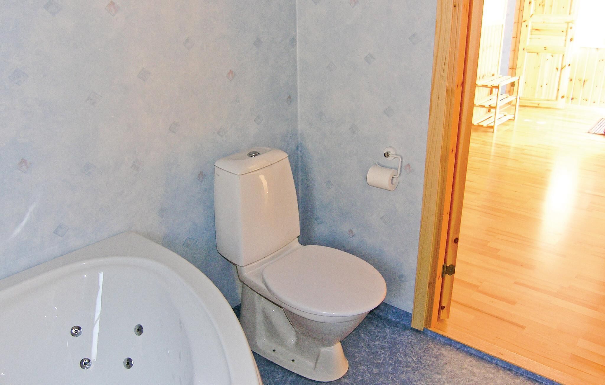 Un baño con inodoro, bañera, suelo de madera y pared con diseño.