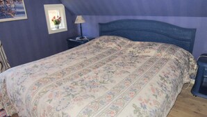Ein Schlafzimmer mit geblümter Bettdecke, einem Nachttisch mit Lampe und einem gerahmten Bild an der Wand.