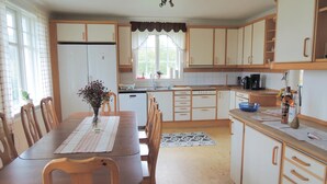 Eine Küche mit Holzschränken, einem Esstisch mit Stühlen, einem Kühlschrank und einem Fenster mit Vorhängen.