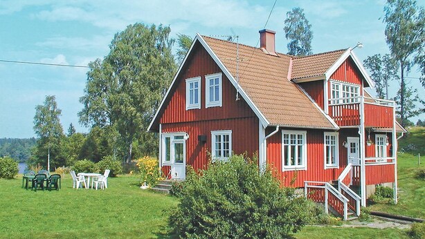 Ein rotes Holzhaus mit einem braunen Dach, einer Veranda und einem kleinen Garten mit Stühlen und Tischen.