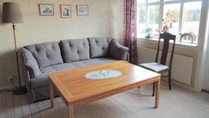 Ein Wohnzimmer mit grauem Sofa, einem Holztisch mit Spitzenunterlage, einem Sessel und einer Heizung.