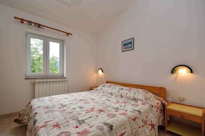 A bedroom with a bed, a window, a radiator, a wall-mounted picture, and bedside lamps. - Holiday apartment 100 m from the beach (Banjole)
