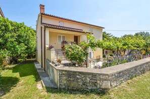 A two-story house with a stone retaining wall, a small balcony, and a garden with flowering plants. - Holiday apartment 100 m from the beach (Banjole)