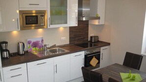 A modern kitchen with white cabinets, a stainless steel microwave, a toaster, and a sink. - 2-room 001 Amrum Terr. Dish washer. (BC 5) - BUE - Apartment house Westwind (Büsum)