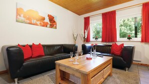 A living room with a black leather sofa, red cushions, a wooden coffee table, and a painting on the wall. - Ferienhaus 6 in Thalfang (Thalfang)