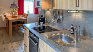 A compact kitchen with a sink, stove, and microwave. There is a dining table with chairs and a vase of flowers. - Ferienhaus 6 in Thalfang (Thalfang)