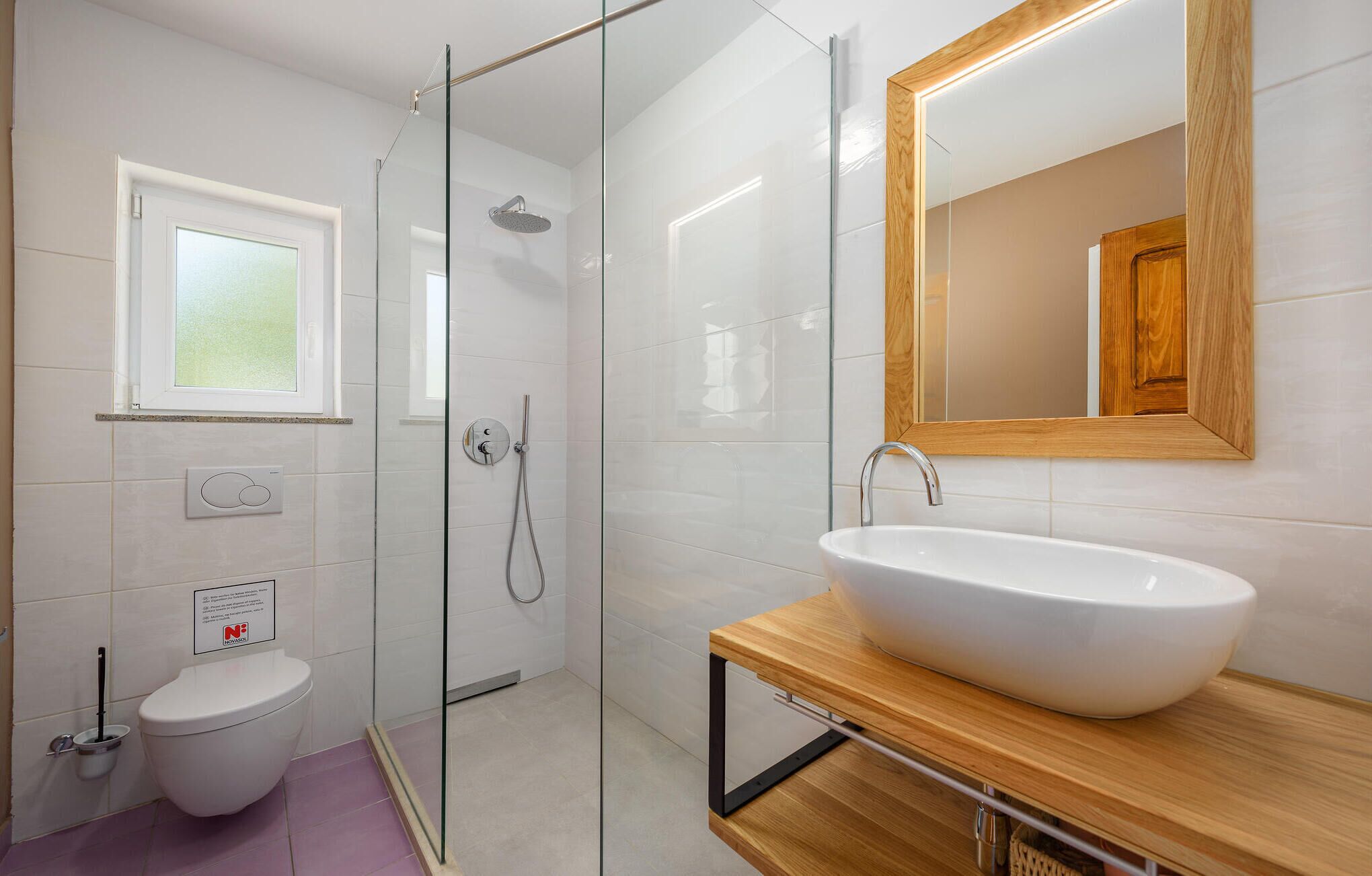 A modern bathroom with a glass-enclosed shower, a white sink, and a wooden vanity.