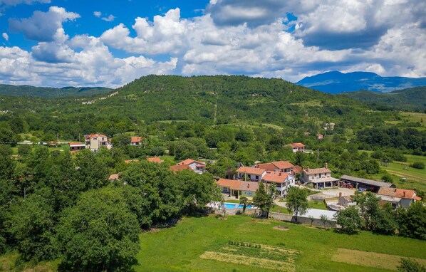 A rural village with houses, a swimming pool, and a mountainous backdrop. - Gorgeous home in Potpican (Potpican)