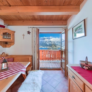 A cozy room with a wooden ceiling, a bench, a table with a checkered tablecloth, a fur throw, a wooden cabinet, and a view of snow-capped mountains through an open door. - Apartment Mondsee - apartment on the farm "Margarethengut" am Attersee (Buchenort)