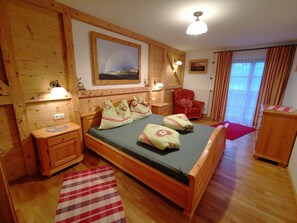 Un dormitorio de madera con una cama, mesitas de noche, una silla y un cuadro en la pared.