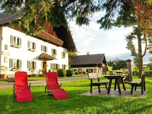 Ein weißes Gebäude mit einem geneigten Dach, einer Veranda und einem kleinen Garten mit Gartenmöbeln.