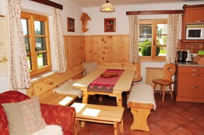 Ein Holzinnenraum mit einer Sitzbank, einem Tisch mit rot-weißer Karotischdecke und einer Küche mit Holzausstattung und einer Mikrowelle.