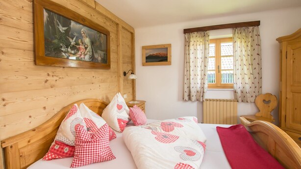 Una habitación de madera con una cama, una ventana con cortinas, un cuadro en la pared y un armario de madera.