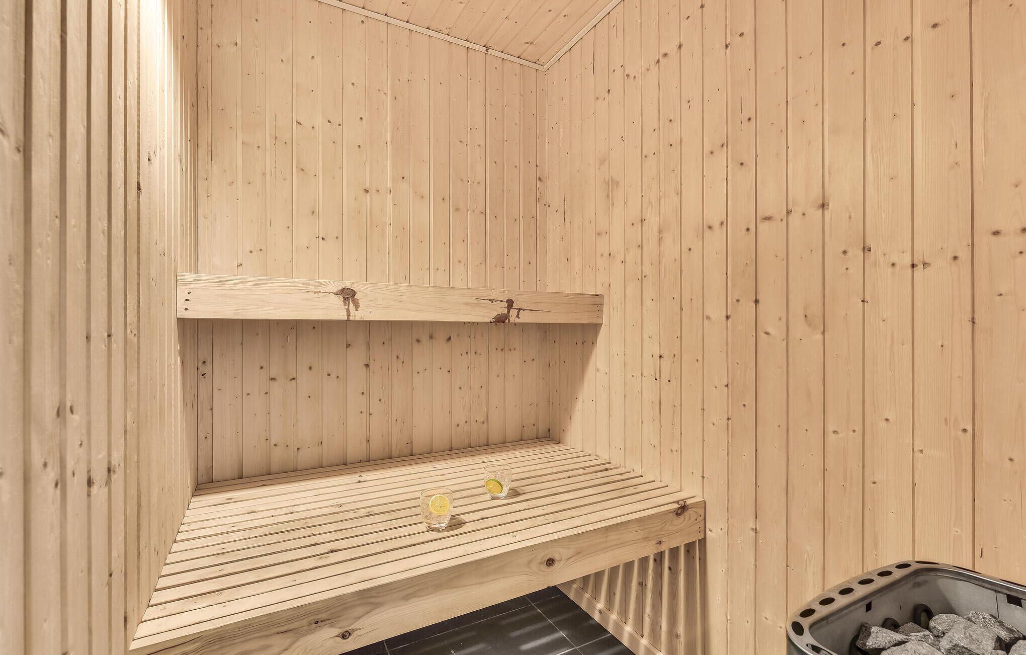 Un cuarto de sauna con paredes y bancos de madera, un lavamanos de metal y un cubo de basura.