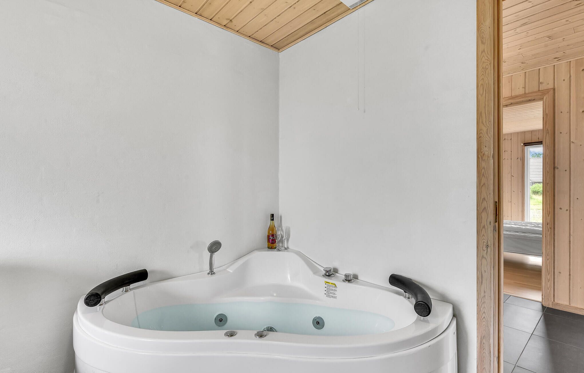 A modern bathroom with a freestanding bathtub, wooden ceiling, and a view of the outside.