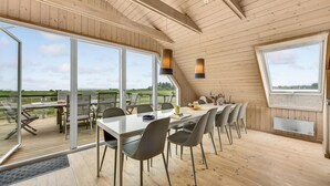 A dining area with a long table and chairs, large windows, and a view of the outdoors. - Amazing home in Skjern with sauna (Skjern)