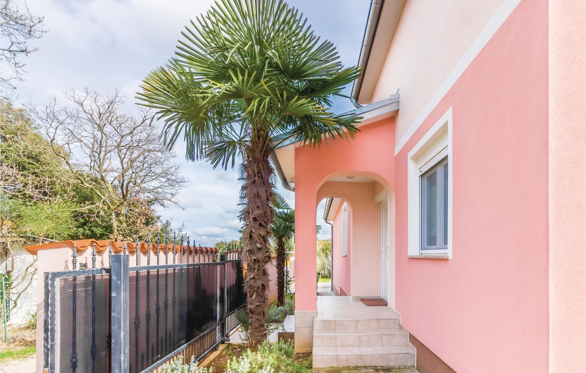 Un edificio rosa con un espacio exterior techado y una palmera.
