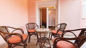 Un pequeño patio con sillas de mimbre y una mesa de vidrio, una puerta blanca y vistas a una habitación con cama y cortinas.