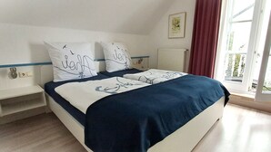 Een slaapkamer met een bed, twee kussens, een nachtkastje, een raam met gordijnen en een radiator.