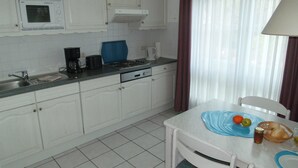 Een keuken met witte kasten, een fornuis, een spoelbak en een eethoek met een tafel en stoelen.