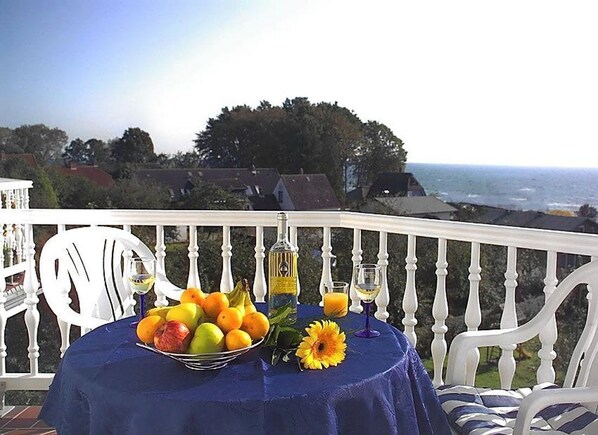 A table with fruit and flowers on a balcony with a view of the ocean.