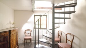 Una escala de caragol en una habitació amb un armari de fusta, dues cadires amb ratlles i una finestra.