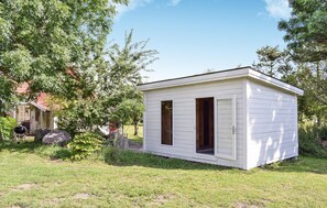 Simple, functional cottage surrounded by lush greenery and a barbecue grill.