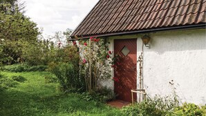 Una casa rústica amb teulada de rajola, una porta de fusta i un petit jardí amb flors vermelles.