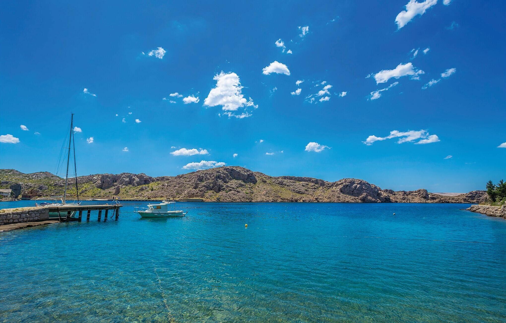 Un lac d’un bleu profond, avec des bateaux amarrés à un quai, le tout entouré de collines rocheuses.
