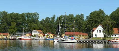 Een jachthaven met aangemeerde boten, een wit gebouw met een rood dak en een bebost achtergrond.