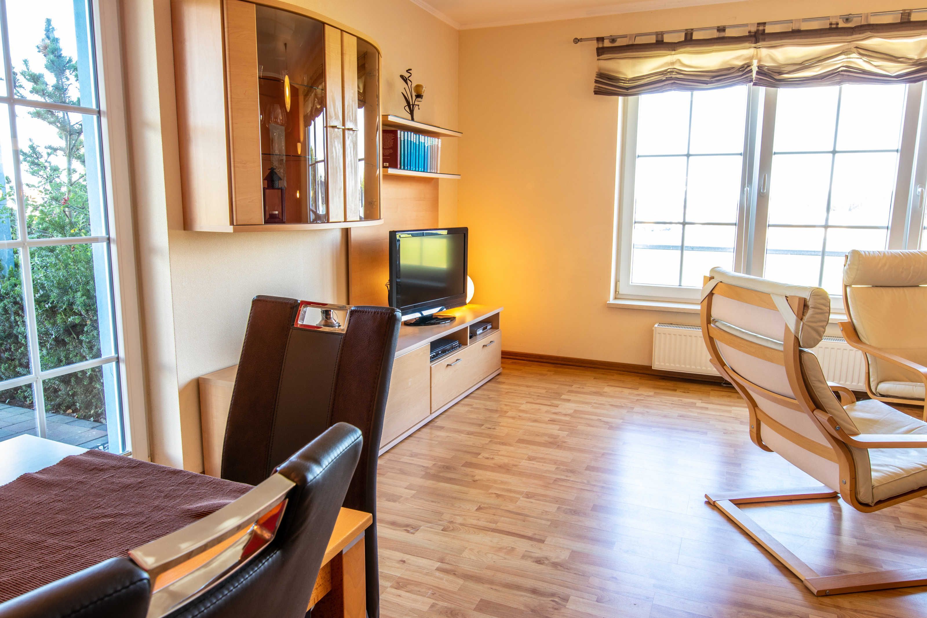 Een woonkamer met een televisie, een bank, een eettafel en een raam met gordijnen.