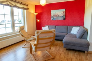Un salon avec un mur rouge, un canapé gris, une chaise en bois et une fenêtre avec des rideaux.