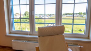A room with a large window, a radiator, and a chair. - Apartment 1 - Apartments in Blu Hus (Kröslin)