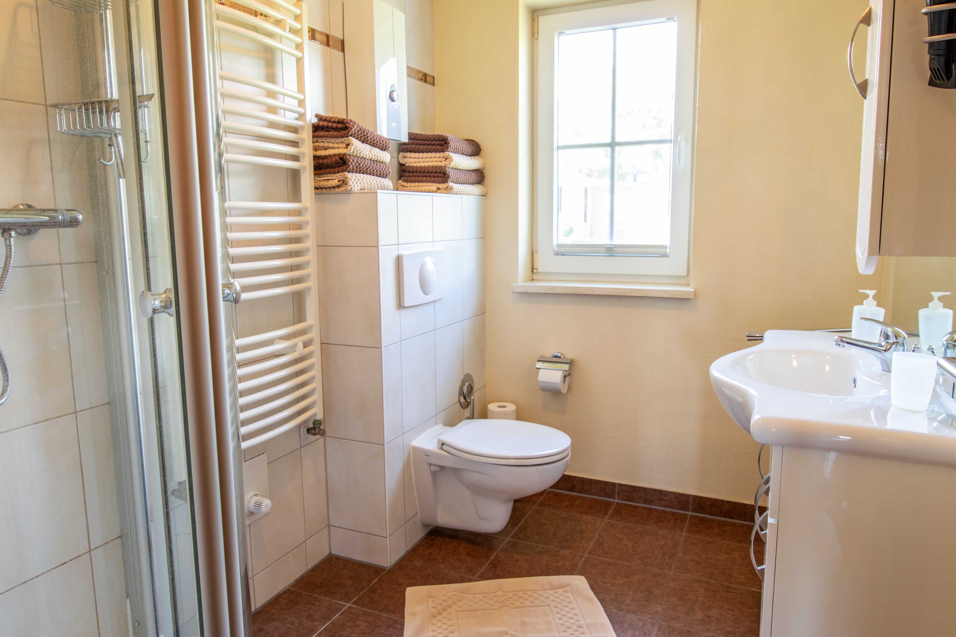 A bathroom with a glass shower enclosure, a toilet, a sink, and a window.