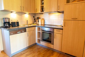 A modern kitchen with wooden cabinets, a dishwasher, a coffee maker, and an oven. - Apartment 1 - Apartments in Blu Hus (Kröslin)