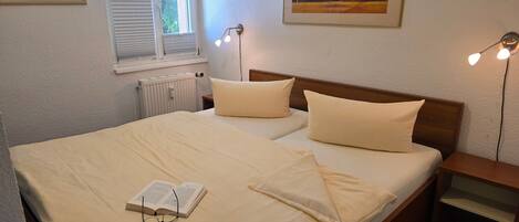 A neatly made bed with pillows and a book, a bedside table, a lamp, and two framed pictures on the wall.