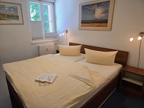 Un lit bien fait, avec des oreillers et un livre, une table de chevet, une lampe et deux tableaux encadrés accrochés au mur.