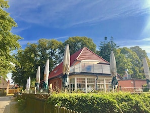 A building with a red-tiled roof, large windows, and outdoor umbrellas. - Vacation apartment Alfredo (Wustrow)