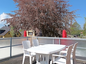 A balcony with a white table and chairs, a red umbrella, and a tree with red leaves. - Vacation apartment Alfredo (Wustrow)