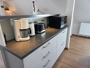 A kitchenette with a coffee maker, toaster, microwave, and a kettle on a speckled countertop. - Vacation apartment Alfredo (Wustrow)